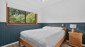 A bedroom with a bed, a nightstand, a lamp, and a window with a view of trees.