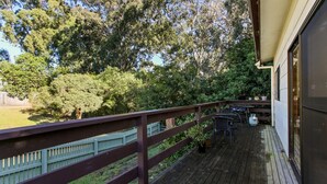 Une terrasse en bois avec une rambarde, des sièges d’extérieur et une vue sur un jardin luxuriant et des arbres.