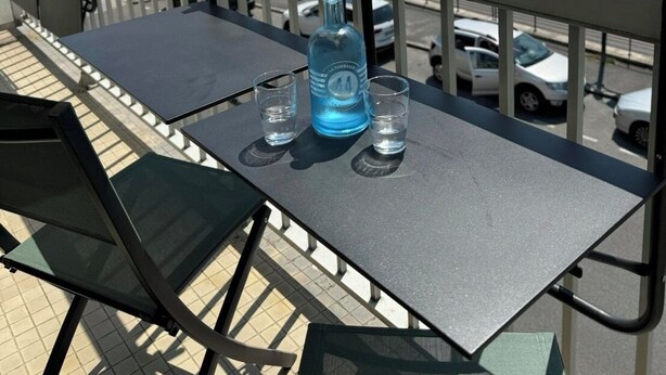 Un balcon avec une table, deux chaises et une bouteille d’eau.