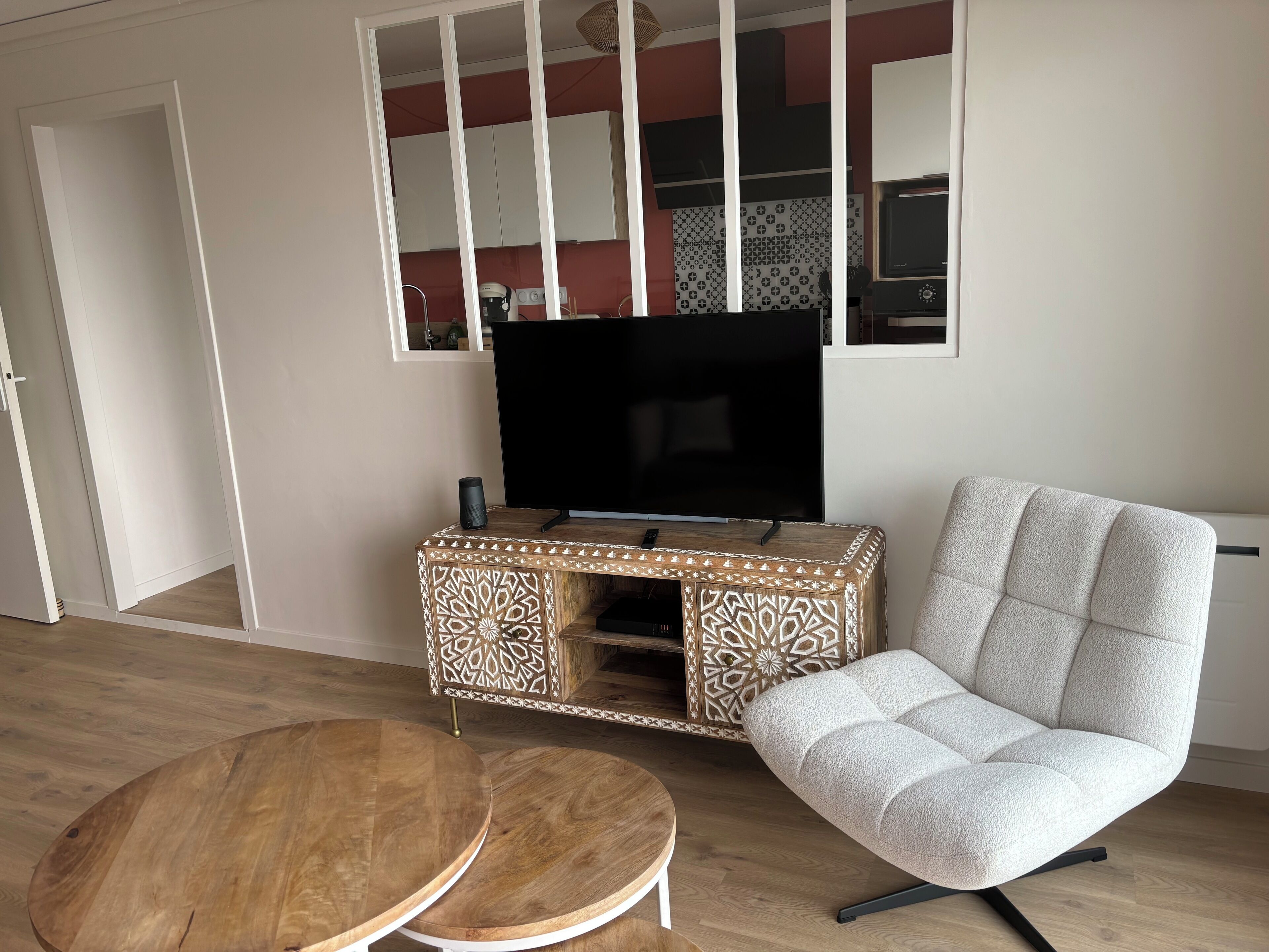 A living room with a TV on a wooden cabinet, a grey sofa, and two round wooden tables.