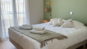 Une chambre à coucher avec un grand lit, une table de chevet, un luminaire suspendu et une fenêtre ornée de rideaux légers.