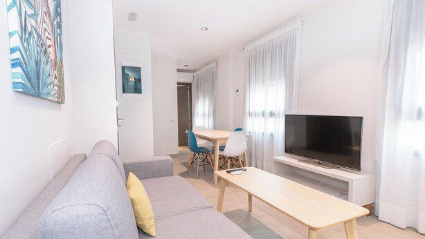 A modern living room with a grey sofa, a wooden coffee table, and a flat-screen TV. - Sholeo Lodges Santa Catalina Flats (Las Palmas de Gran Canaria)