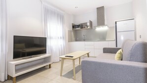 A modern living room with a flat-screen TV, a grey sofa, a wooden coffee table, and a kitchen area with a microwave and refrigerator. - Sholeo Lodges Santa Catalina Flats (Las Palmas de Gran Canaria)