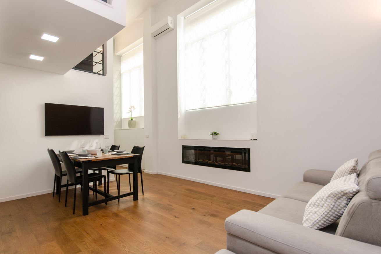A modern living room with a dining area, a fireplace, and a large window.