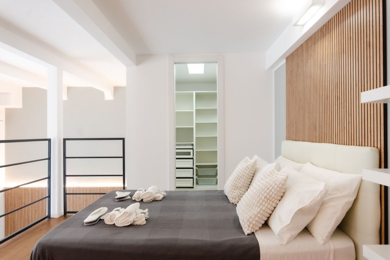 Een moderne slaapkamer met een bed, een inbouwkleerkast en uitzicht op een wand van houten latten.