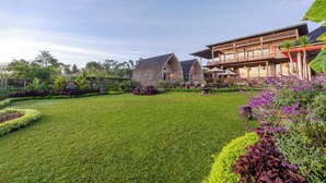 A well-maintained lawn, a large building with a curved roof, and a dining area with outdoor seating. - Mountain Healing Villa by Nagisa Bali (Baturiti)