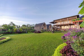 A well-maintained lawn, a large building with a curved roof, and a dining area with outdoor seating. - Mountain Healing Villa by Nagisa Bali (Baturiti)