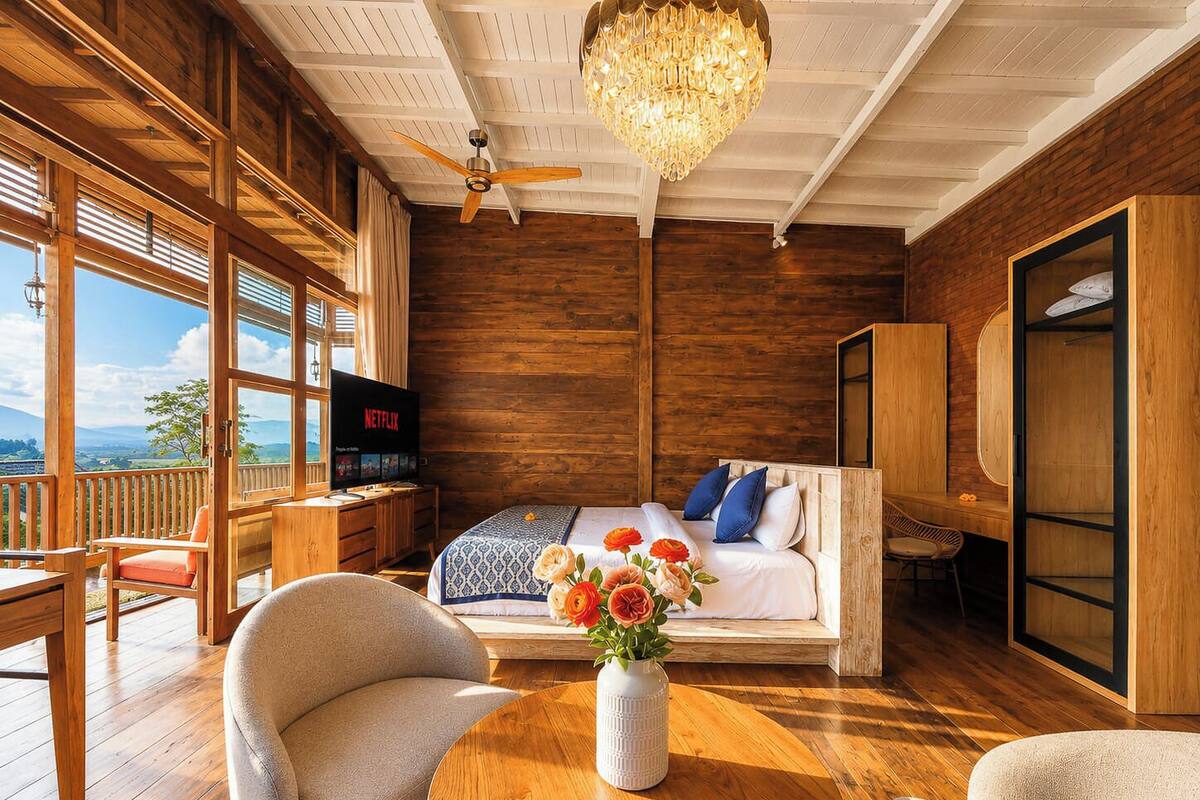 A bedroom with a bed, a TV, a wooden desk, and a balcony.