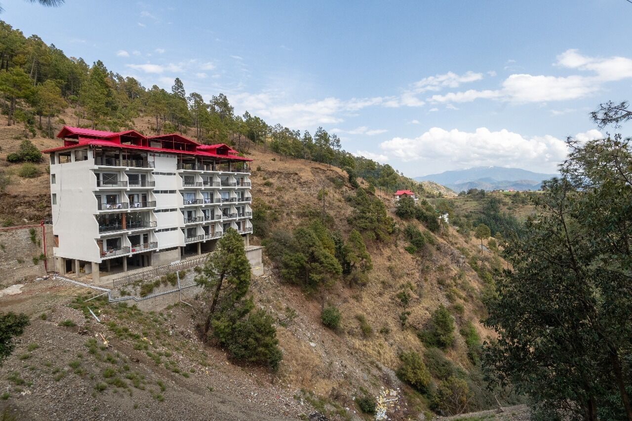 Een meerhoog hotel met balkons, gelegen op een heuvel met uitzicht op het omliggende landschap.