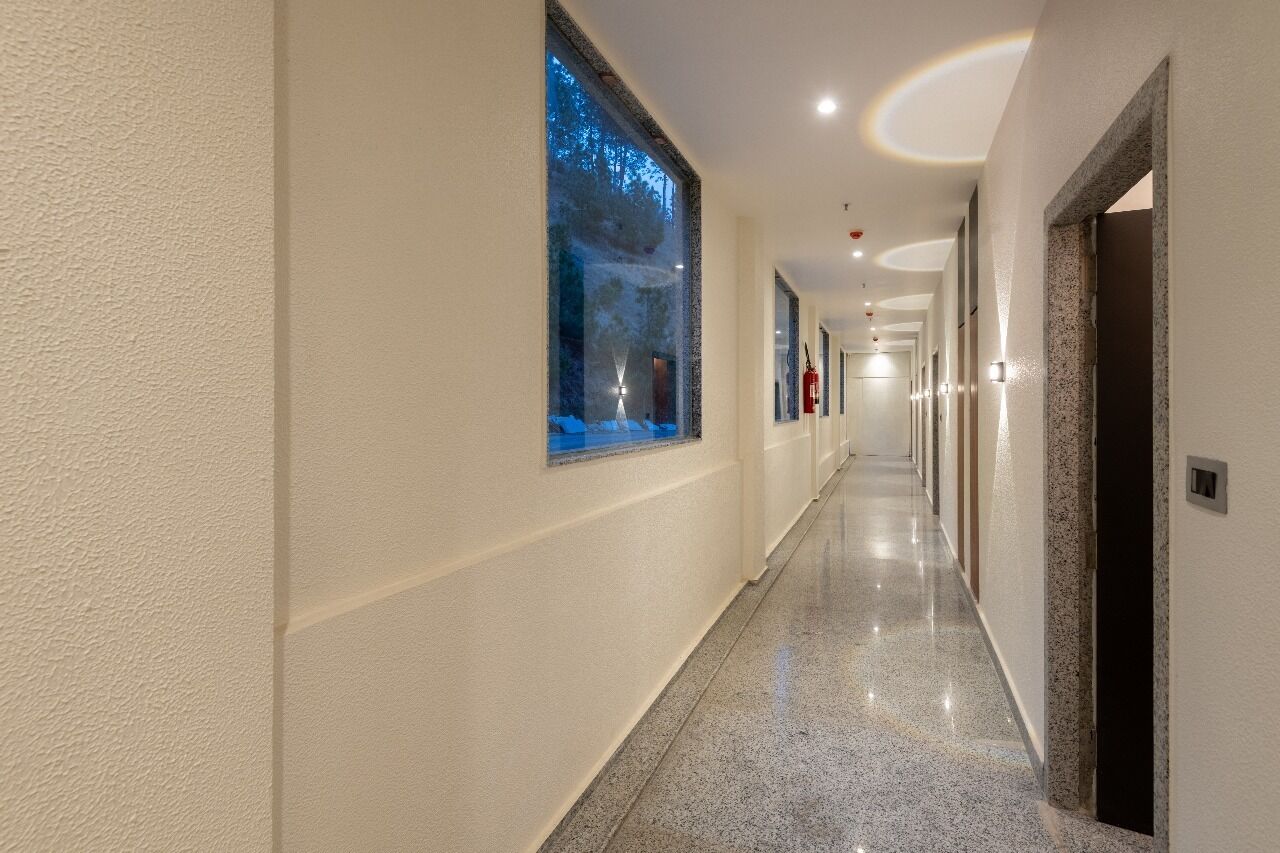 A long, well-lit hallway with a polished floor, a large window with a view of trees, and a fire extinguisher mounted on the wall.