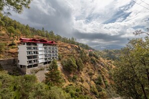 A multi-story hotel with balconies, situated on a hillside with a view of a mountainous landscape. - Kavin The Chail Resort - Serene Valley Views (Kandaghat)
