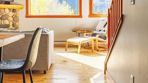 A room with a large window offering a mountain view, a wooden dining table, a sofa, and a chair. - Ha Ling Haven - Penthouse with Shared Rooftop Hot Tub (Canmore)
