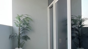 Ein Balkon mit künstlichem Grünrasen, zwei Kübelpflanzen und einer Schiebetür.