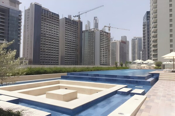 A modern urban setting with high-rise buildings, a swimming pool area with steps, and construction cranes in the background.