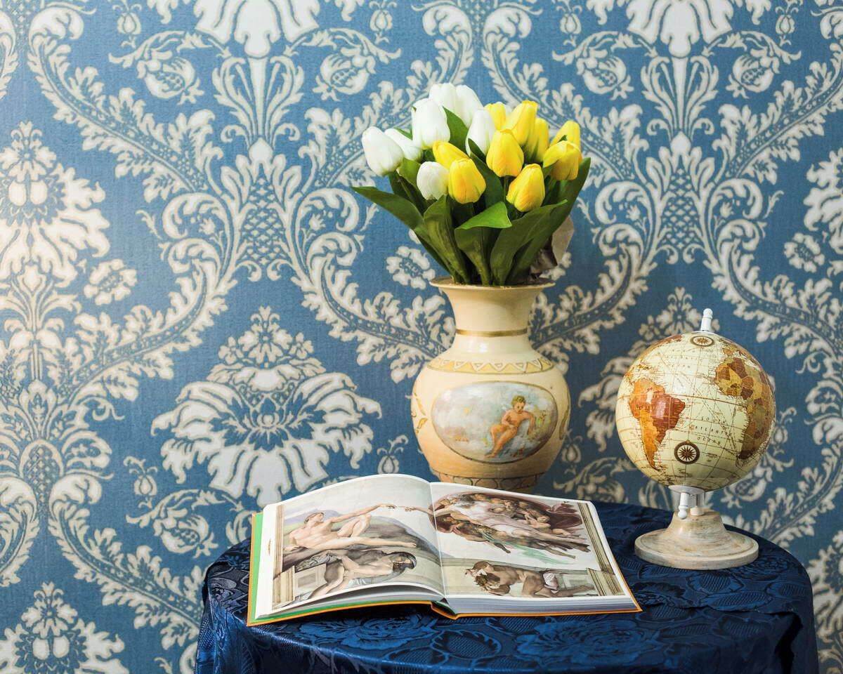 A book, a globe, and a vase with flowers on a table against a patterned wallpaper.