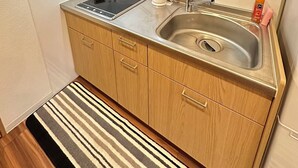 A compact kitchen with wooden cabinets, a stainless steel sink, a kettle, and a built-in induction cooktop.