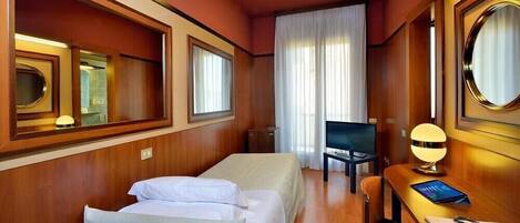 A hotel room with a bed, a desk with a lamp, a TV, and a large mirror.