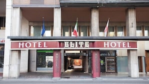 A hotel facade with 'HOTEL ELITE' signage, multiple flags, and a grand entrance.