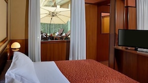 A hotel room with a bed, a television, and a view of an outdoor area with a table and chairs.