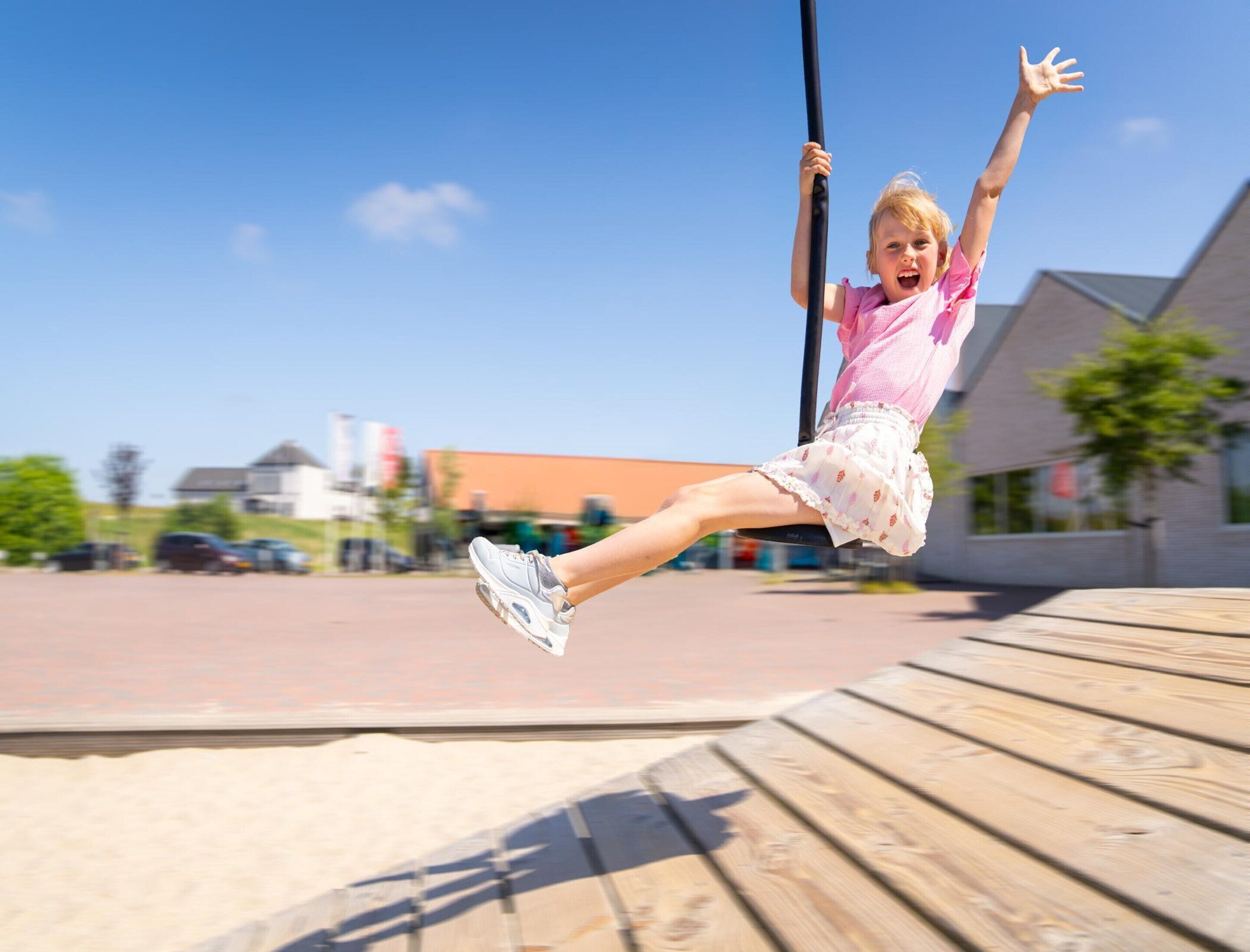A child on a swing in an outdoor setting with buildings in the background.