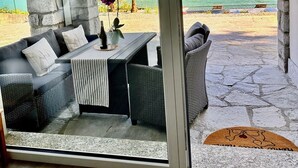 Ein zeitgemäßer Außenbereich mit Sitzgelegenheit, einer Steinsäule, einer gepolsterten Couch und einem Tisch mit einer Vase und einer Weinflasche.
