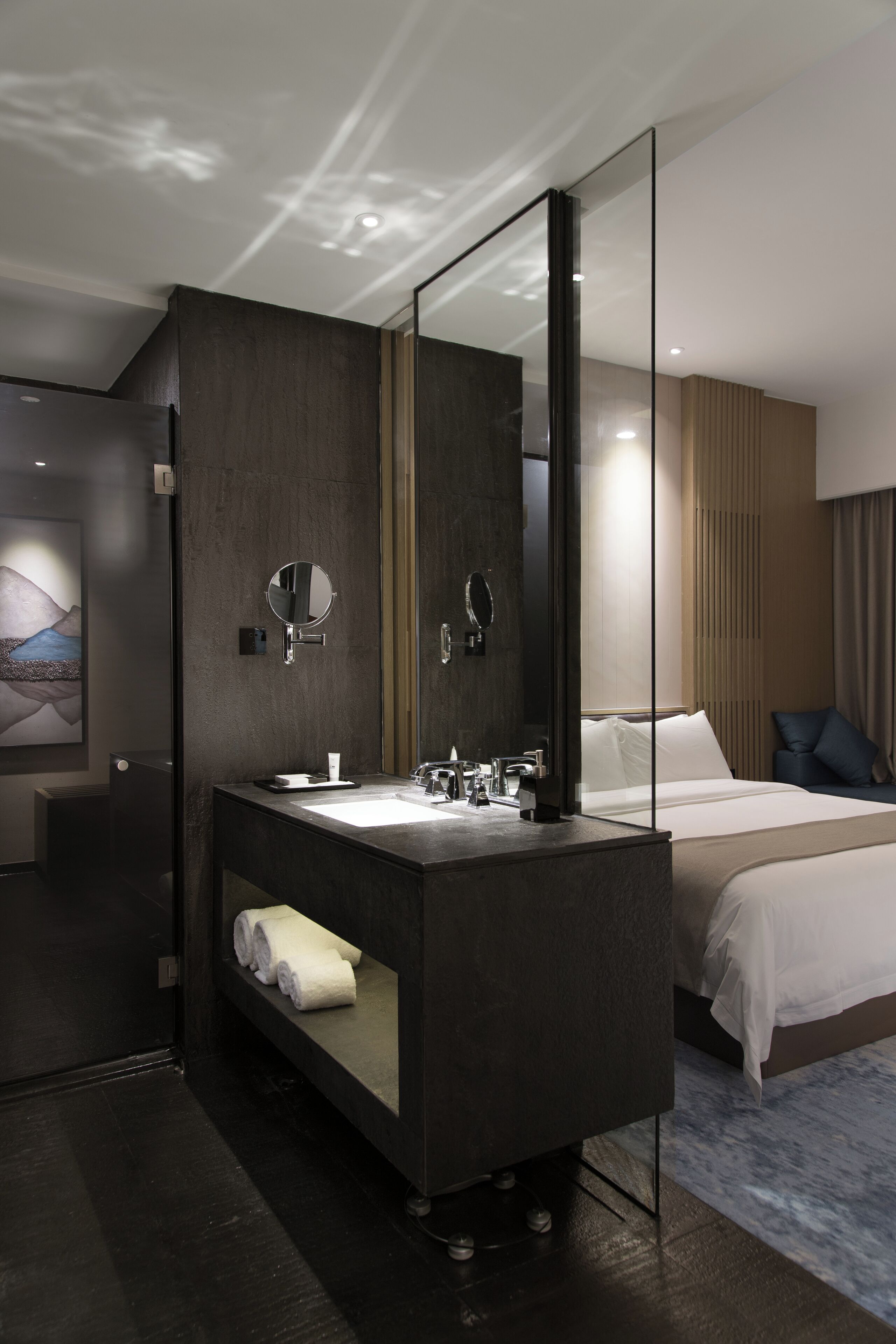 Ein modernes Hotelzimmer mit einem dunklen Holz-Waschtisch, einem großen Spiegel, einem Bett mit weißen Bettbezügen und Blick auf die Stadtlandschaft durch das Fenster.