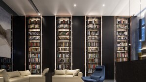 A modern library with a sectional sofa and a blue chair, surrounded by tall bookshelves. - Zhonghao International Hotel  (Dongguan)