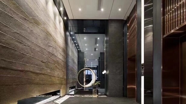 A modern hallway with a stone wall, a circular sculpture, and a sleek elevator. - Zhonghao International Hotel  (Dongguan)