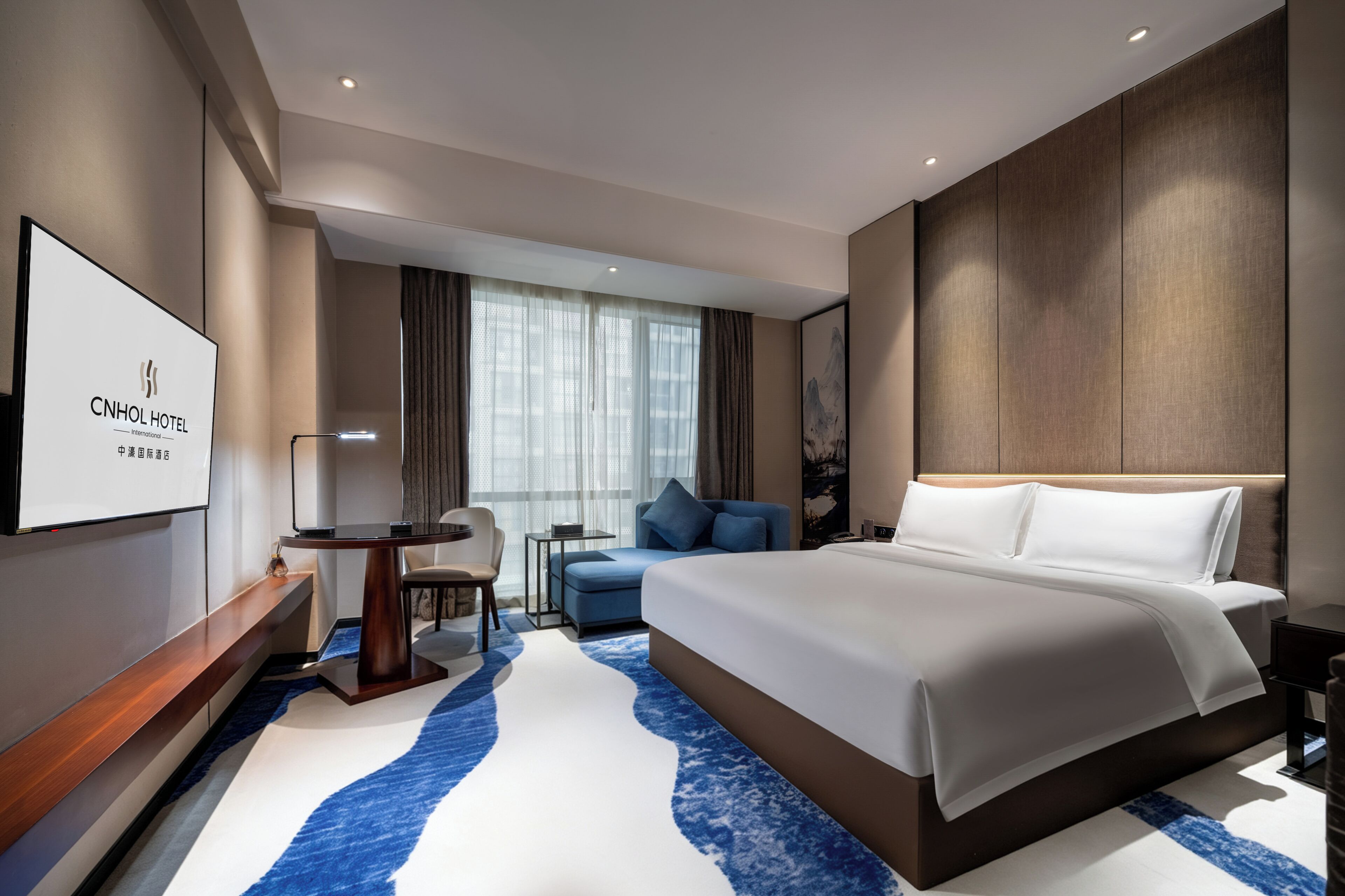 Ein modernes Hotelzimmer mit einem großen Bett, einem Schreibtisch, einem Stuhl und einem Fernseher.
