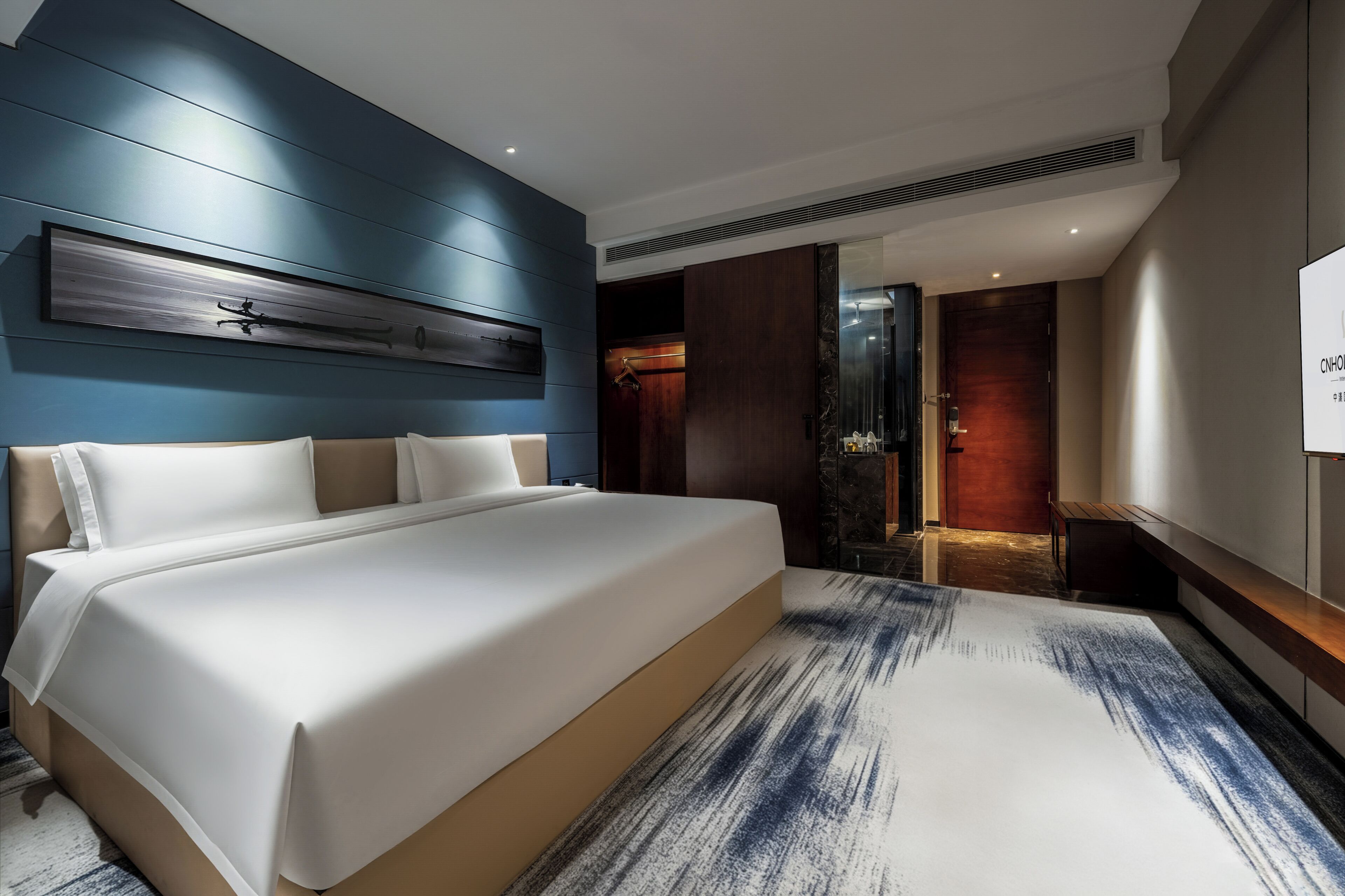 Une chambre d’hôtel moderne avec un grand lit, un mur d’accent bleu et une œuvre d’art contemporaine au-dessus du lit.