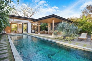 A modern house with a swimming pool, outdoor seating, and a covered patio area.
