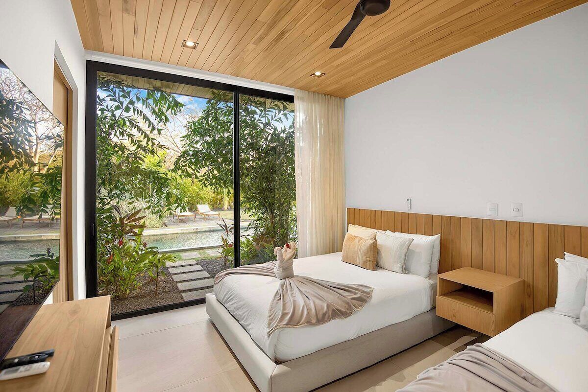 Een moderne slaapkamer met een groot bed, een houten hoofdbord en uitzicht op een tuin door een schuifdeur.