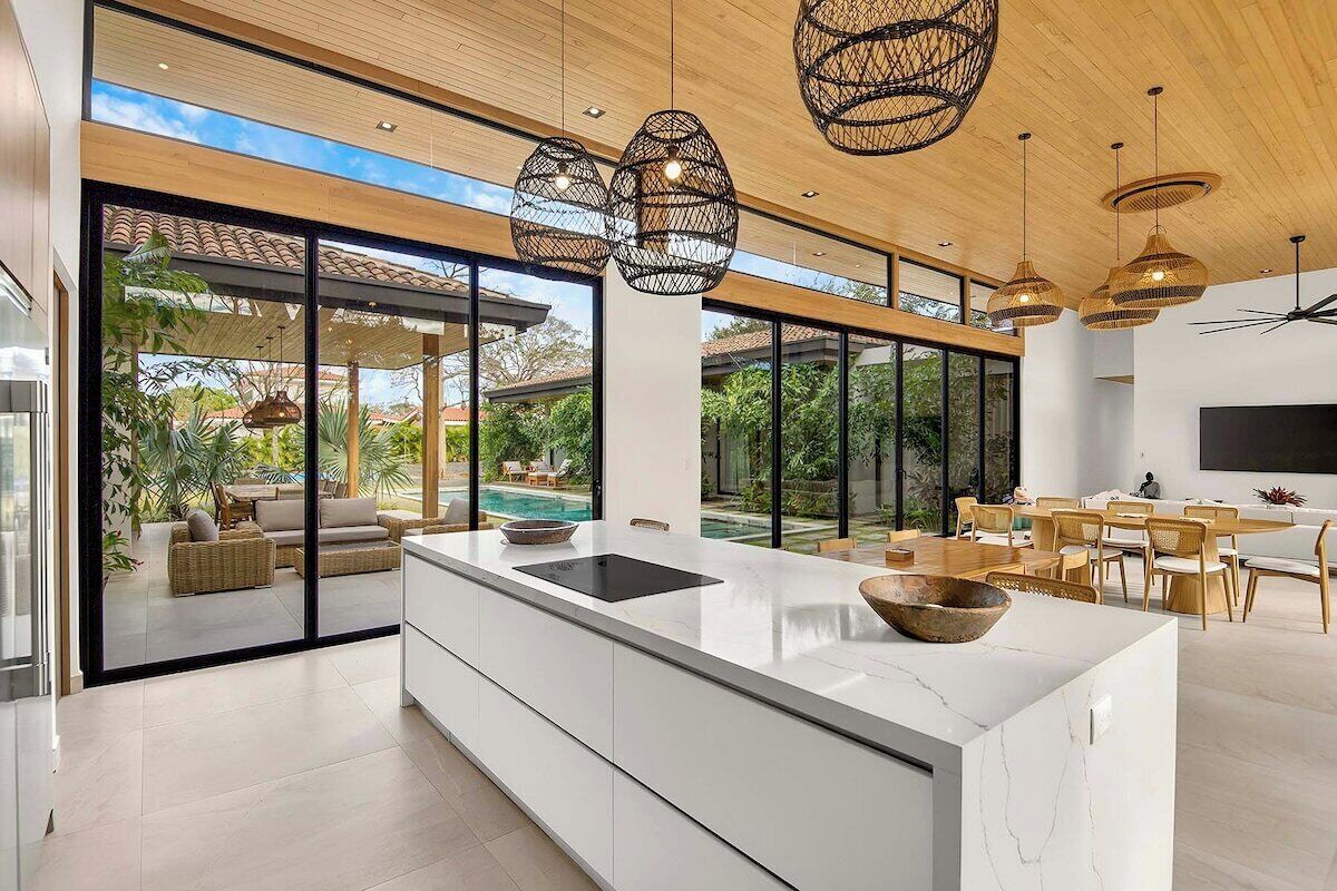 Une cuisine moderne dotée d’un grand îlot central, de grandes fenêtres et d’un coin repas avec des meubles en bois.