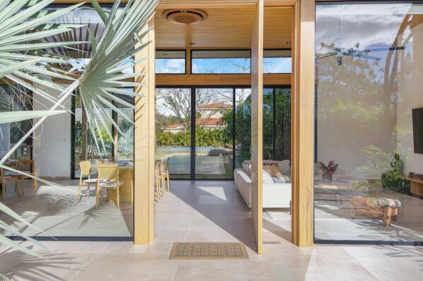 A modern interior with a glass door leading to a pool area, wooden furniture, and a view of the outdoors.