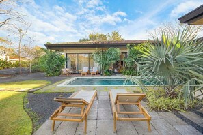 Een modern huis met een zwembad, terras en weelderige beplanting.