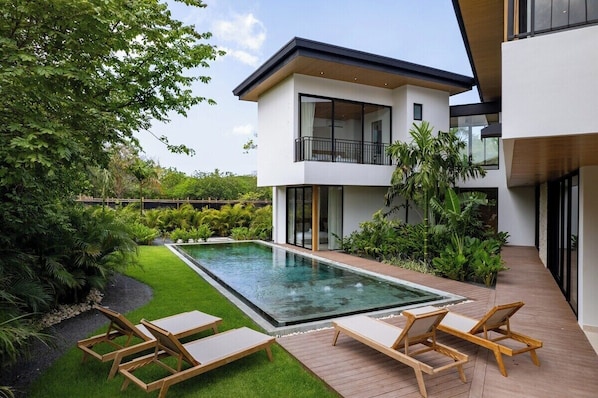 A modern two-story house with a swimming pool, outdoor seating, and lush greenery.
