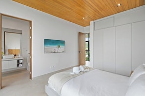 A bedroom with a large bed, a wooden ceiling, a painting, and a bathroom with a sink and mirror.