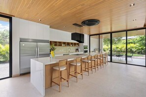 Une cuisine moderne dotée d’un îlot central, de tabourets de bar et offrant une vue sur la verdure environnante.