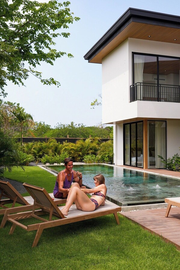 A modern house with a swimming pool, a covered patio, and lush greenery.