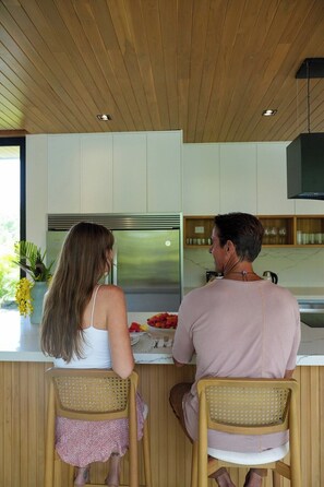 A modern kitchen with wooden cabinets, a stainless steel refrigerator, and a dining area with wicker chairs.