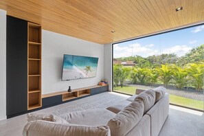 A modern living room with a large window, a flat-screen TV, and a sofa.