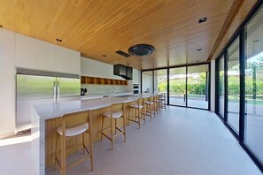 A modern kitchen with a long counter, bar stools, and large windows.