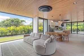 A modern interior with a curved sofa, dining area, and large windows overlooking greenery.