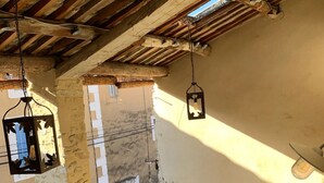 An outdoor patio with a round table and chairs, wooden beams, hanging lanterns, and a view of buildings in the background. - Logis de Charlise (Vallabrix)