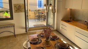 A modern kitchen with a wooden countertop, a dining area with a table set for four, and a view of the outdoor patio. - Logis de Charlise (Vallabrix)