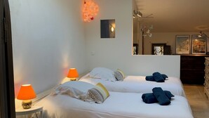 A bedroom with two beds, a skylight, a small table with a lamp, and a patterned rug. - Logis de Charlise (Vallabrix)