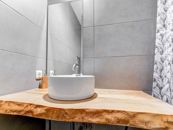 A modern bathroom with a wooden vanity, a white sink, and a large mirror.