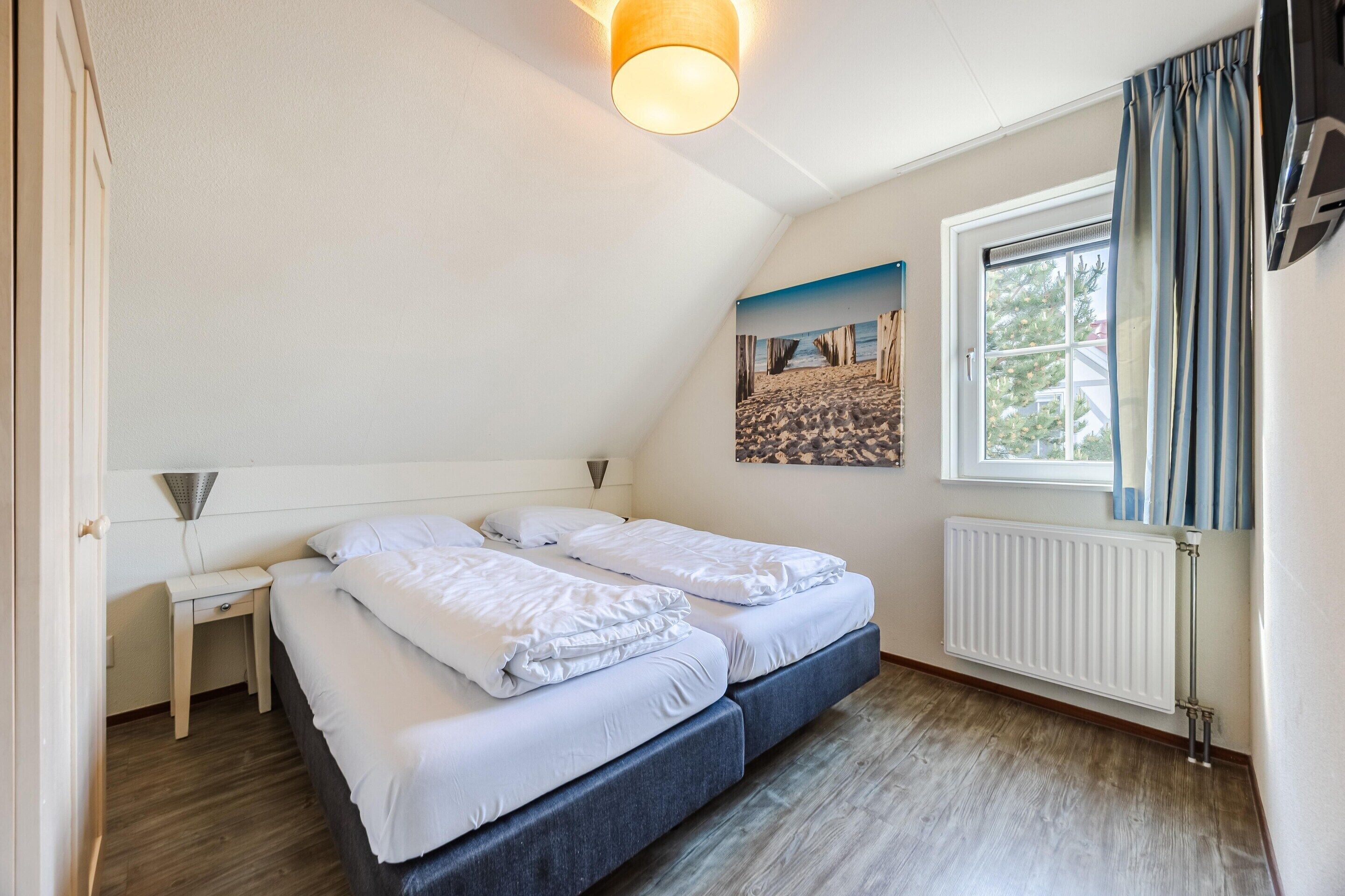 A room with two beds, a window with curtains, a radiator, and a painting on the wall.