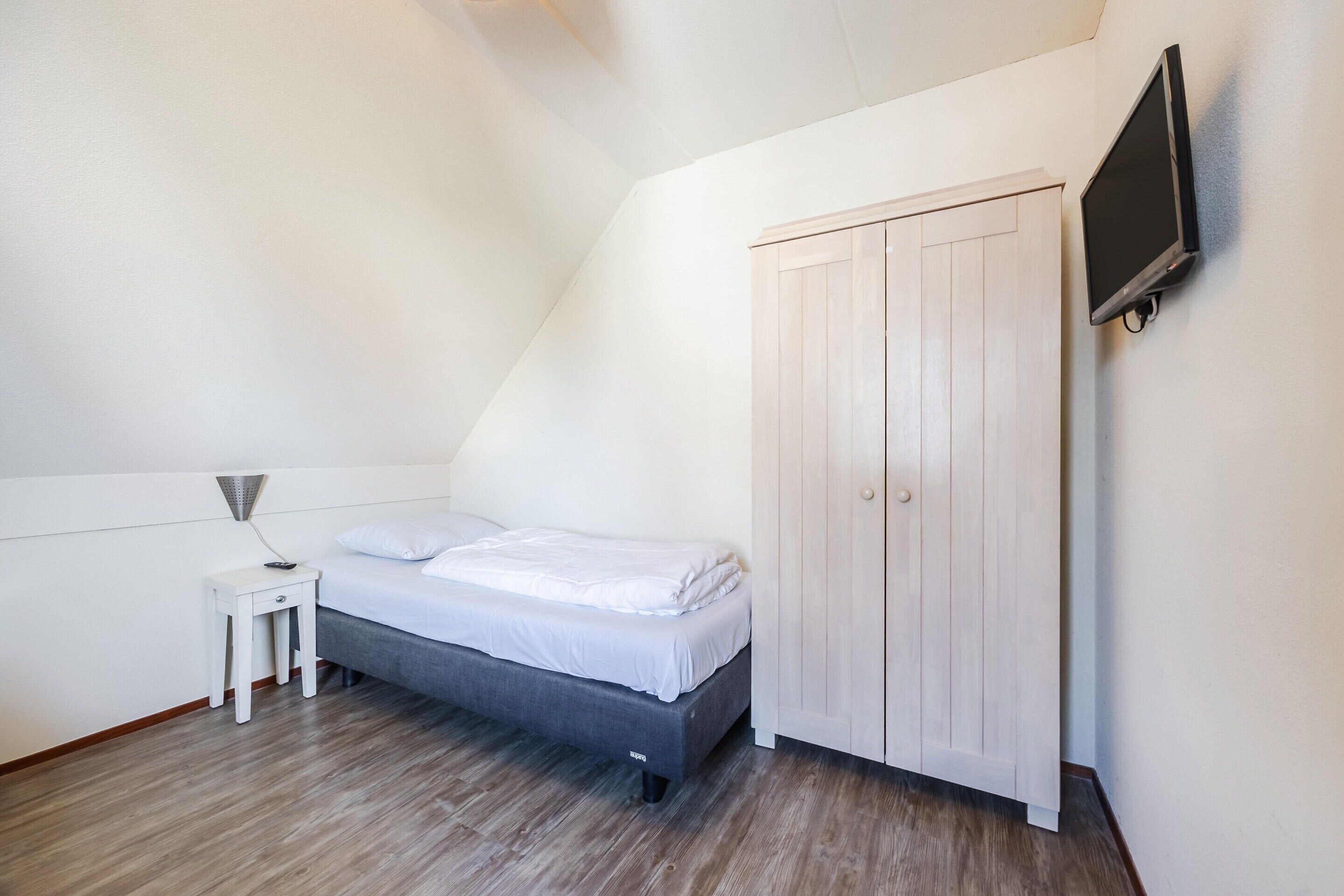 Une chambre à coucher comprenant un lit, une petite table de chevet, un téléviseur fixé au mur et une armoire.