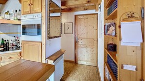 A wooden interior with a kitchen area, wooden cabinets, a radiator, and a door with a label. - Copalme - appartement - 5/7 pers - Centre (Les Gets)